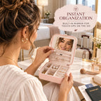 Woman using a blush pink travel jewelry organizer with built-in mirror while placing a pearl earring at a hotel vanity