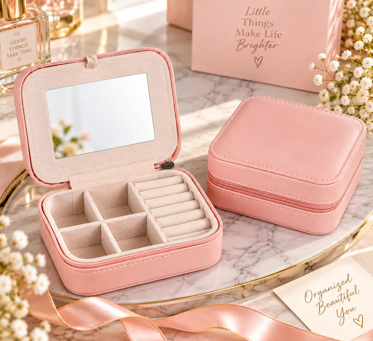 Blush pink travel jewelry organizer with built-in mirror and divided velvet compartments displayed open beside a closed matching case on a marble vanity