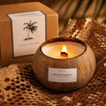CAPRI&COOL natural coconut shell aromatherapy candle with a lit wooden wick on honeycomb kraft paper beside a premium kraft gift box