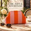Orange and blush pink striped knitted clutch on a sunlit café table with sunglasses, white rose, coffee and book